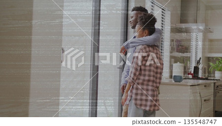 Embracing couple gazing through sliding glass door in kitchen with mug plant utensils, copy space Embracing couple gazing through sliding glass door in kitchen with mug plant utensils, copy space 135548747