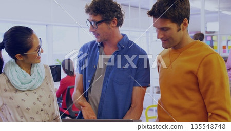 Collaborating colleagues reviewing project on laptop in open plan office, colorful sticky notes 135548748