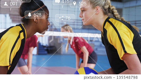 Facing off teenage players in yellow-black jerseys holding volleyball over net at sports hall Facing off teenage players in yellow-black jerseys holding volleyball over net at sports hall 135548798