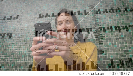 Holding smartphone, man in mustard sweater tapping through data overlays against mosaic tile wall Holding smartphone, man in mustard sweater tapping through data overlays against mosaic tile wall 135548837