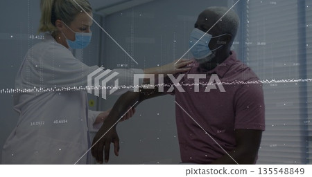 Assessing doctor in lab coat supporting patient arm at clinic, with surgical masks and exam chair Assessing doctor in lab coat supporting patient arm at clinic, with surgical masks and exam chair 135548849
