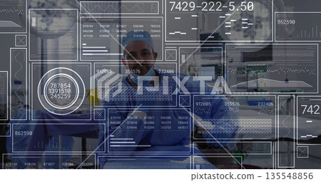 Analyzing digital panels, male surgeon in blue scrubs and cap in operating room with tools 135548856