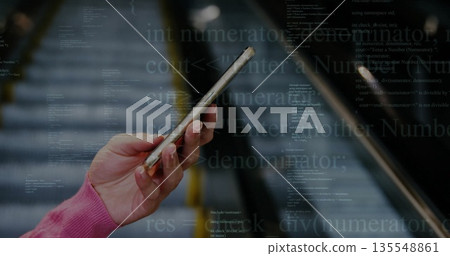 Holding smartphone hand in pink long sleeves on moving escalator, with floating code overlay 135548861