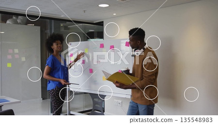 Gesturing woman and man discussing Concept diagram on whiteboard in meeting room, with sticky notes 135548983