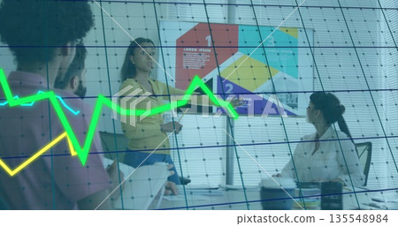 Presenting woman in yellow top and jeans explaining graphs on flip chart in office meeting room 135548984