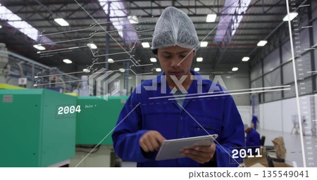 Tapping tablet, male technician monitoring machines in factory hall, wearing coveralls 135549041