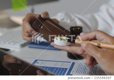 Medical team having a meeting with doctors in white lab coats and surgical scrubs seated at a table discussing a patients working online using computers in the medical industry. 135549107