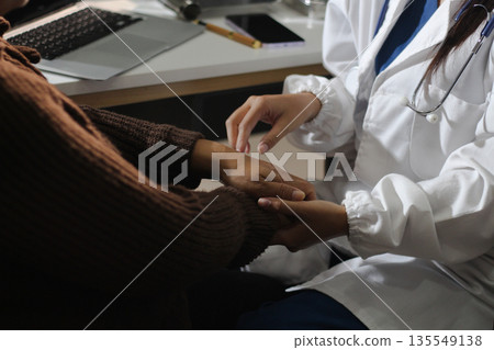 Senior patient lying in hospital bed receiving comforting touch from young female nurse, hands gently clasped together, medical care setting visible 135549138