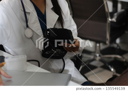 A doctor's hands carefully taking a patient's blood pressure using a sphygmomanometer. A doctor's hands carefully taking a patient's blood pressure using a sphygmomanometer. 135549139