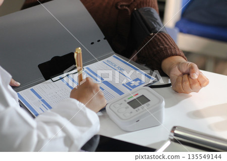 A doctor's hands carefully taking a patient's blood pressure using a sphygmomanometer. A doctor's hands carefully taking a patient's blood pressure using a sphygmomanometer. 135549144