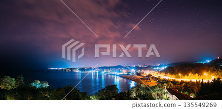 Mediterranean Bay Night Panorama – Illuminated Coastal Settlement with Palm Trees and Water 135549269