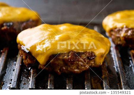 Melting cheese on a beef burger patties grilling a hot barbecue grill. 135549321