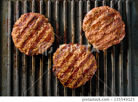 Beef burger meat patties grilling on a barbecue grill, top view. Beef burger meat patties grilling on a barbecue grill, top view. 135549325