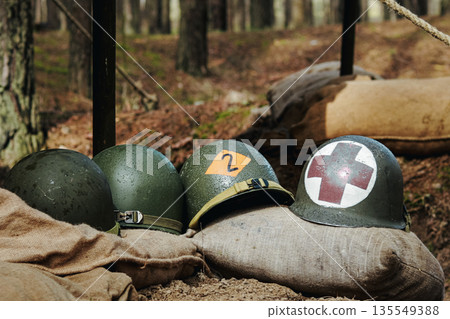 WWII American Metal Helmets Of United States Army Infantry Soldier At World War II. Helmets Near Camping Tent In Forest Camp WWII American Metal Helmets Of United States Army Infantry Soldier At World War II. Helmets Near Camping Tent In Forest Camp 135549388