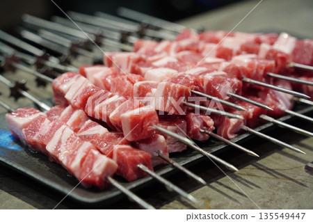 Raw, uncooked lamb skewers on a grill, a popular Chinese barbecue street food, ready for cooking. 135549447