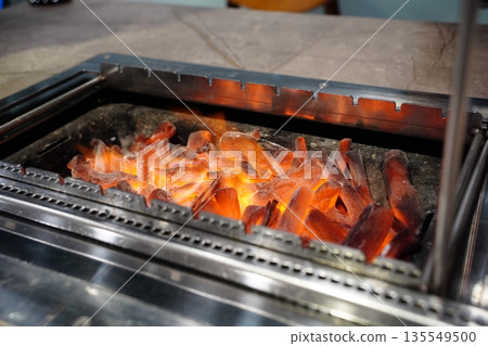 Close-up of burning charcoal embers in an automatic rotating lamb skewer bbq grill machine. Close-up of burning charcoal embers in an automatic rotating lamb skewer bbq grill machine. 135549500
