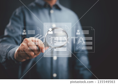Businessman analyzing digital resumes with magnifying glass for recruitment process 135549563