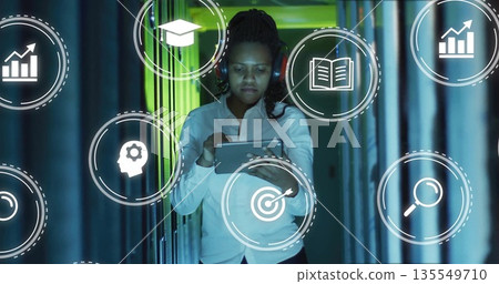 Tech professional woman tapping tablet in server rack corridor, showing floating analytics icons Tech professional woman tapping tablet in server rack corridor, showing floating analytics icons 135549710