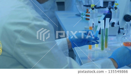 Handling technician hands wearing blue gloves positioning test tube rack on lab bench with pipettes Handling technician hands wearing blue gloves positioning test tube rack on lab bench with pipettes 135549866