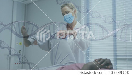 Woman doctor in lab coat and mask lifting patient leg in examination room, with DNA overlay 135549908