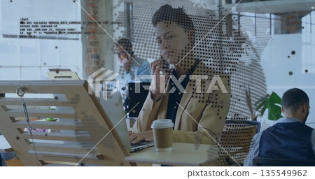 Talking Black woman typing on laptop while holding smartphone in open-plan office with coffee Talking Black woman typing on laptop while holding smartphone in open-plan office with coffee 135549962