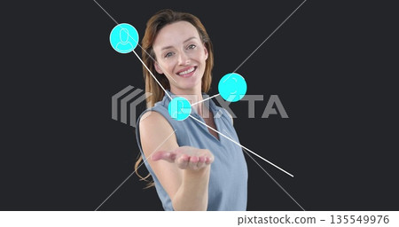 Presenting mid adult female extending palm toward camera in studio, with turquoise icons Presenting mid adult female extending palm toward camera in studio, with turquoise icons 135549976