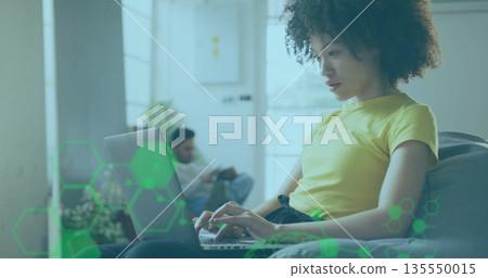 Typing woman using laptop in living room, with potted plant and man using smartphone, copy space 135550015