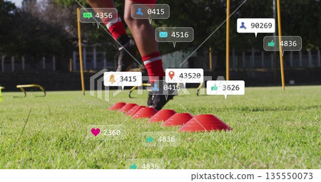 Athlete weaving in red socks and cleats on grass field, with red cones, poles, floating icons Athlete weaving in red socks and cleats on grass field, with red cones, poles, floating icons 135550073