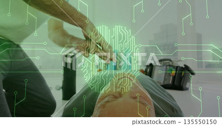 Kneeling man in green shirt holding defibrillator paddles over senior chest in room with AED unit 135550150