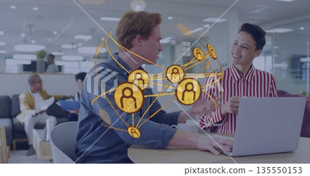 Typing two office workers collaborating at shared workspace with silver laptop and network graphic Typing two office workers collaborating at shared workspace with silver laptop and network graphic 135550153