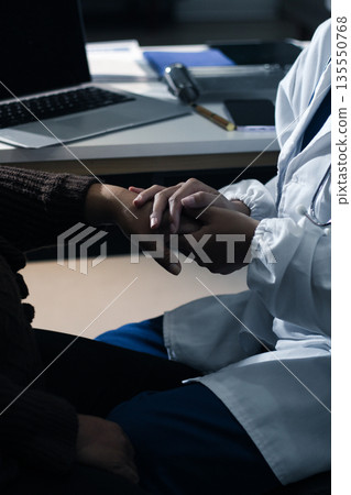 Senior patient lying in hospital bed receiving comforting touch from young female nurse, hands gently clasped together, medical care setting visible Senior patient lying in hospital bed receiving comforting touch from young female nurse, hands gently clasped together, medical care setting visible 135550768