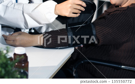 A doctor's hands carefully taking a patient's blood pressure using a sphygmomanometer. A doctor's hands carefully taking a patient's blood pressure using a sphygmomanometer. 135550772