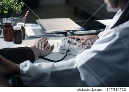A doctor's hands carefully taking a patient's blood pressure using a sphygmomanometer. A doctor's hands carefully taking a patient's blood pressure using a sphygmomanometer. 135550780