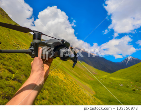 Adult man holding drone in mountainous region during sunny day Adult man holding drone in mountainous region during sunny day 135550978