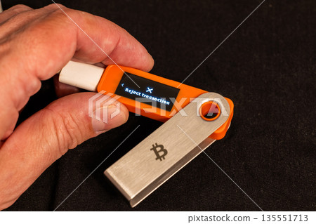 Male hand holding hardware wallet with reject transaction option on its screen 135551713