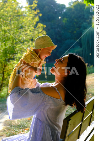 Mother Lifting Baby Outdoors in Sunny Park 135552023