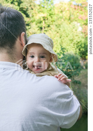 Smiling Baby in Beige Hat Held by Adult Outdoors 135552027