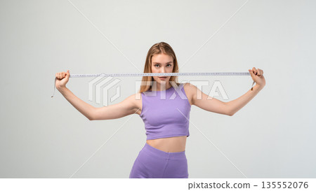 Fit woman stretching measuring tape in studio, body size check, diet and fitness progress concept with copy space background 135552076