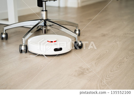 Robotic vacuum cleaner cleaning office floor under rolling chair, smart home appliance for automated daily household maintenance Robotic vacuum cleaner cleaning office floor under rolling chair, smart home appliance for automated daily household maintenance 135552100