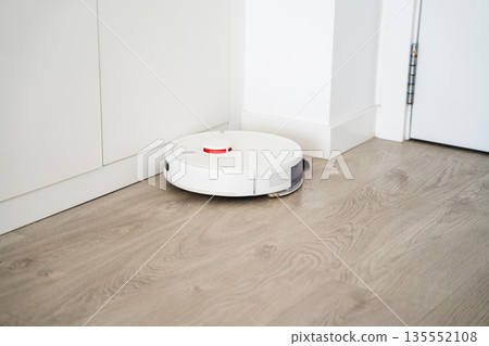 Smart robotic vacuum cleaner cleaning corner near wall and door in modern apartment with automated household technology Smart robotic vacuum cleaner cleaning corner near wall and door in modern apartment with automated household technology 135552108