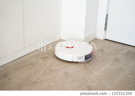 Smart robot vacuum cleaner cleaning floor near washing machine in modern kitchen with automated home cleaning technology 135552109