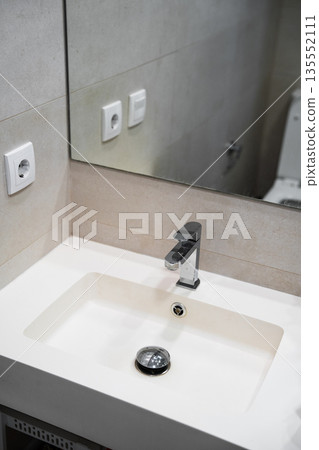 Modern bathroom vanity corner with white sink and chrome faucet, minimalist tiled wall and mirror, home interior and plumbing design concept Modern bathroom vanity corner with white sink and chrome faucet, minimalist tiled wall and mirror, home interior and plumbing design concept 135552111
