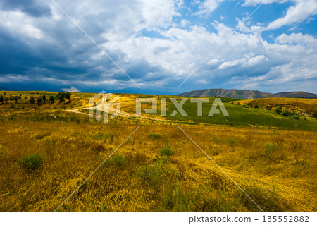 Rolling hills and dirt road under cloudy sky in autumnal Kyrgyzstan Rolling hills and dirt road under cloudy sky in autumnal Kyrgyzstan 135552882