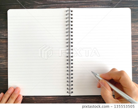 Female hands writing in a notebook on a wooden table Female hands writing in a notebook on a wooden table 135553505