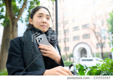 A woman wearing a scarf and using a smartphone A woman wearing a scarf and using a smartphone 135553597