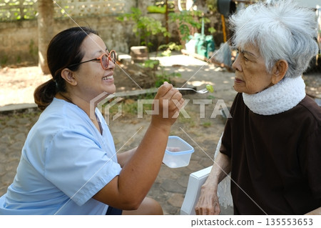 The caregiver is feeding fruit to the elderly person. The caregiver is feeding fruit to the elderly person. 135553653