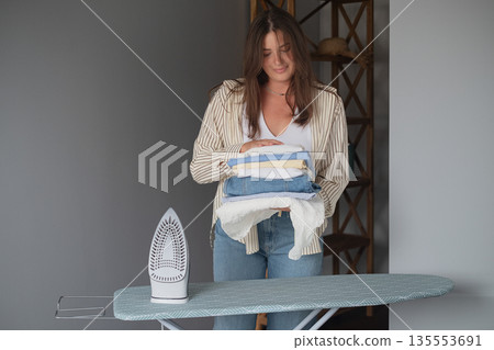 Woman in home clothes neatly stacks steamed clothes preparing them for wardrobe showing home routine and organized living 135553691