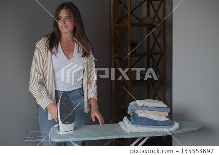 Household chores concept with girl in home clothes ironing laundry and neatly stacking it on a calm home day 135553697