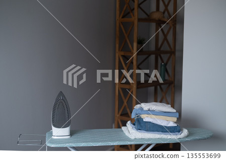 Everyday home comfort with iron on ironing board as a symbol of neatness and order in the household Everyday home comfort with iron on ironing board as a symbol of neatness and order in the household 135553699