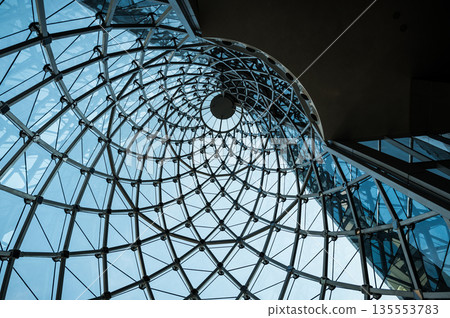 Modern blue glass roof with spiral shape made from connecting steel with blue sky as background. Modern blue glass roof with spiral shape made from connecting steel with blue sky as background. 135553783